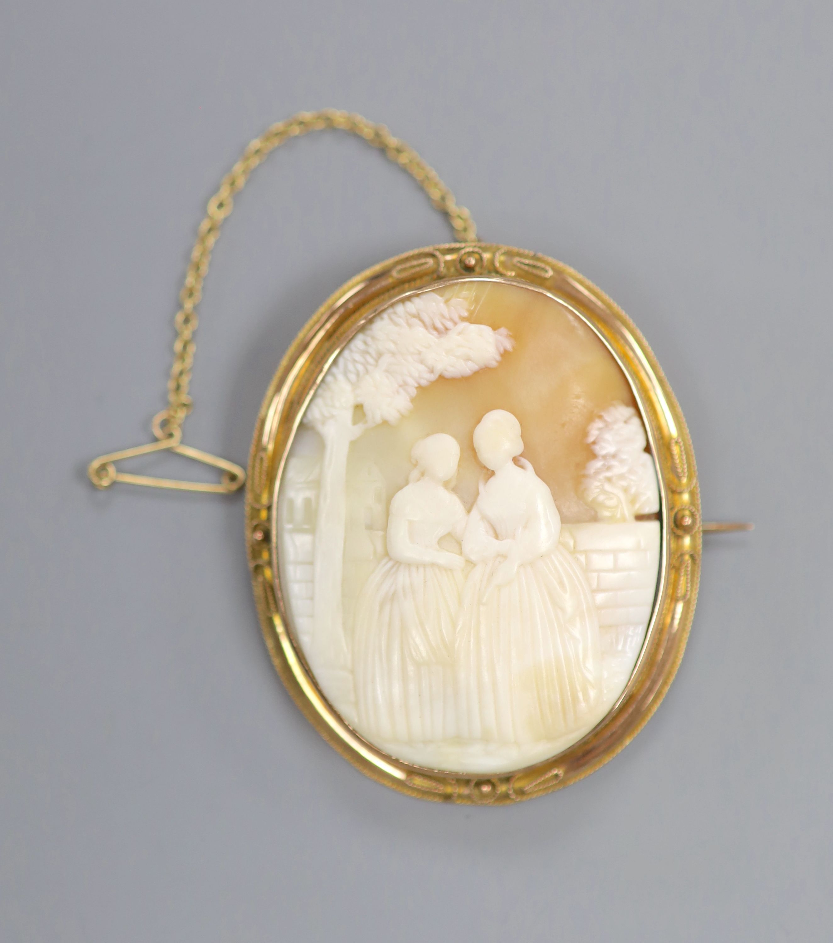 A yellow metal mounted oval cameo shell brooch, carved with scene of two ladies in a garden, 55mm, gross 19.3 grams.